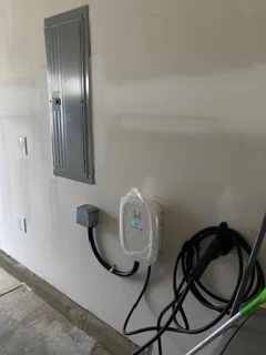 Wall-mounted EV charger with white faceplate and organized black power cables on drywall