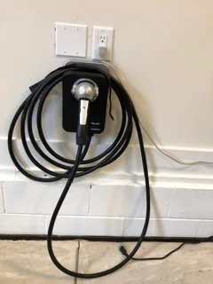 Level 2 EV charger with black cable coiled on white wall-mounted outlet box