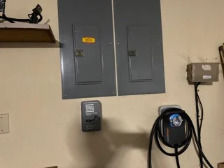 Gray electrical panels, EV charger unit, and black charging cable mounted on interior wall