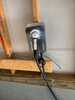 Black EV charger mounted on wall with cable management and wooden framing visible