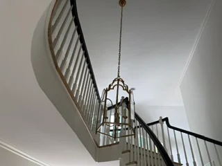 Brass pendant light fixture suspended in stairwell with metal railings and white ceiling